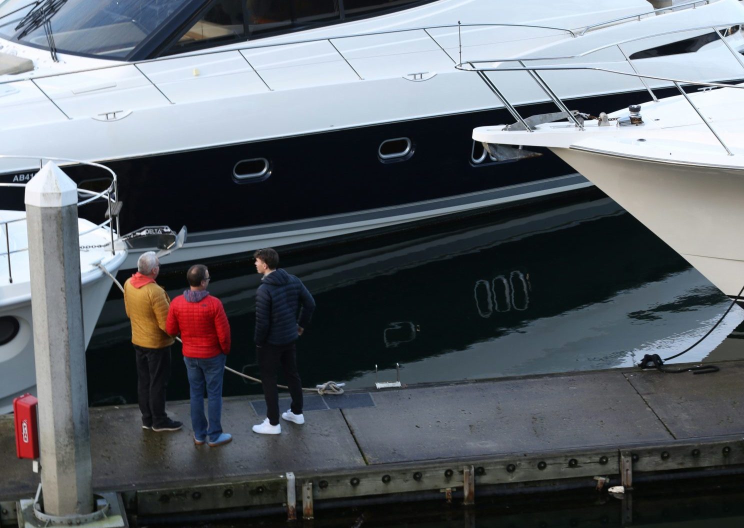 Three people stand on a dock next to yachts